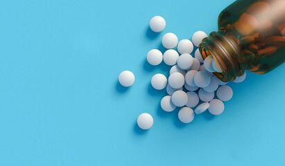 White tablets spilling out of a glass bottle isolated on blue backdrop with space for text. 3d illustration top down view. © Paulista