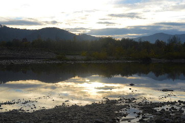 Beautiful landscape with high mountains with illuminated peaks, stones in mountain lake, reflection, blue sky and yellow sunlight in sunrise.
