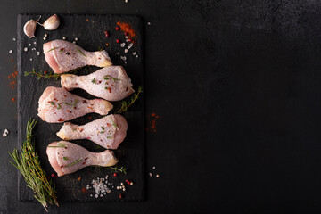raw chicken drumsticks with spices and herbs on black board