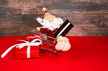 Decorative Christmas elf or gnome in shopping trolley holding a credit card. Background with christmas gift boxes.
