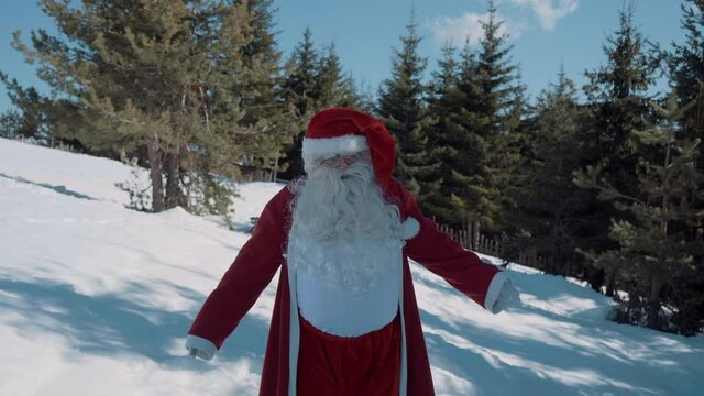 Santa walks with outstretched arms to the camera on a snowy field.
