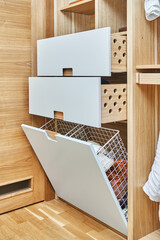 Modern wardrobe with opened metal mesh laundry basket and wooden drawers. Wooden wardrobe with light gray cabinet doors