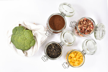 Fresh broccoli in an eco friendly beige tote bag on white background. Glass jars with green tea,granola, coffee, pasta. Zero waste concept, flatly.