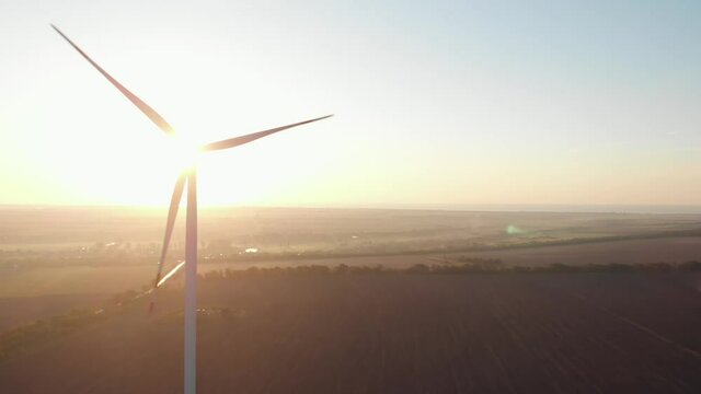 Wind turbines power plant aerial sunset view green energy. Wind mills rotating generating renewable energy at golden hour light flares