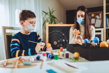 Happy school boy and girl with protective mask making a solar system for a school science project at home