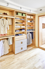 Modern wardrobe with clothes hanging on slide out racks and folded on the shelves. Modern furniture