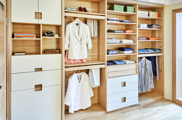 Modern wardrobe with clothes hanging on slide out racks and folded on the shelves. Modern furniture