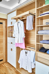 Modern wardrobe with clothes hanging on slide out racks and folded on the shelves. Modern furniture