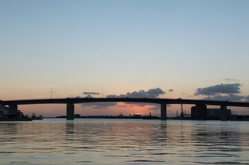 Obraz na płótnie Canvas オレンジ色の夕焼けとシルエットの高架橋のある凪の港
