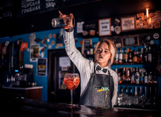 Confident girl barman intensely finishes his creation at bar