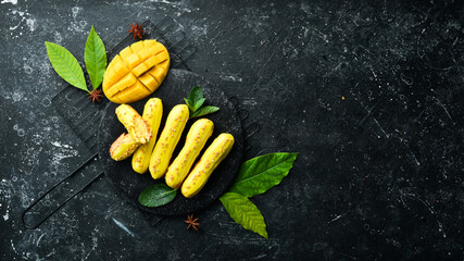 Eclair with mango cream. Mango dessert on a black stone plate. Top view. Rustic style.