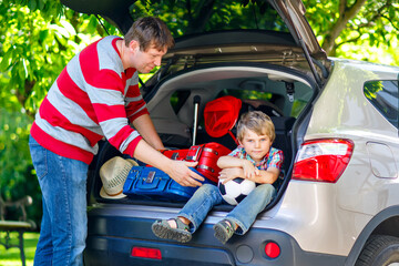 Little kid boy sitting in car trunk just before leaving for summer vacation. Dad packing suitcases. Happy family going on long journey during ockdown and quarantine time due corona pandemic disease