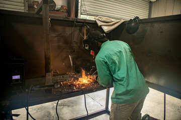 A man welds two pieces of metal together in a shop with an arc welder.