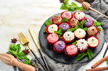 Set of colored cream muffins on a black plate with mint. Top view. Rustic style.