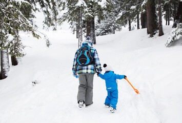 Two unrecognizable people, a dad with a little son, in warm overalls, are walking through the snowy forest. back in the frame. winter family vacation in the mountains, active lifestyle