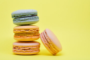 Multicolored macaroons in the form of a tower on a yellow background. Colorful greeting card with delicious almond cookies. Sponge cakes on top of each other. Spaces for text, copy space.