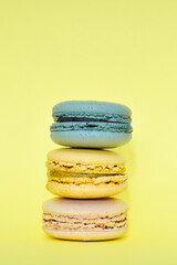 Multicolored macaroons in the form of a tower on a yellow background. Colorful greeting card with delicious almond cookies. Sponge cakes on top of each other. Spaces for text, copy space.