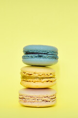 Multicolored macaroons in the form of a tower on a yellow background. Colorful greeting card with delicious almond cookies. Sponge cakes on top of each other. Spaces for text, copy space.