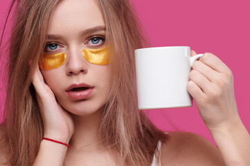 Woman with headache and hangover holding cup with hot drink on pink isolated background