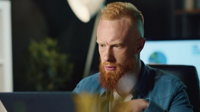 Focused hipster guy filling data on computer in night office. Man looking screen