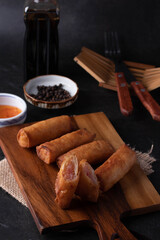 Fried spring rolls with dipping sauce on a wooden cutting board
