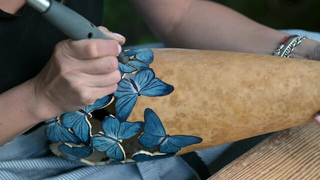 A young woman using an etching tool to trace a handmade craft decorated with butterflies