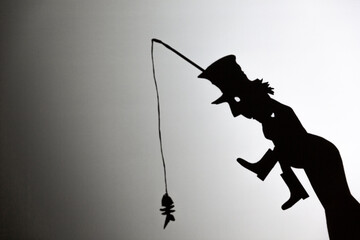play shadow projected against a white background. a homeless man with a rod fishing
