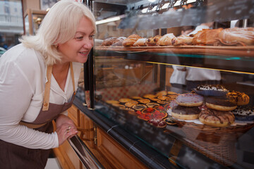 Lovely mature female baker examining her retail display at her bakery store