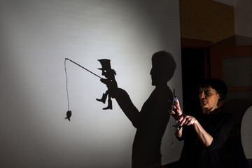 play shadow projected against a white background. a homeless man with a rod fishing