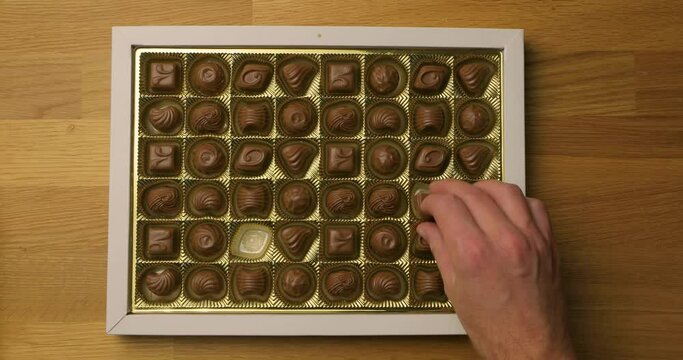 Box of chocolate bonbon candies put on a table and hands taking pieces