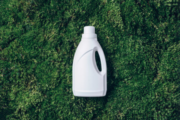 White plastic bottle of cleaning product, household chemicals or liquid laundry detergent on green...