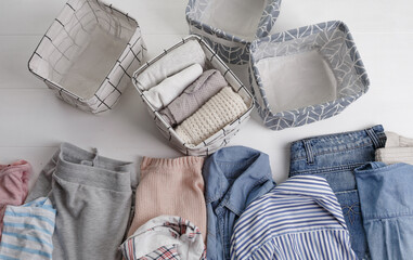 A group of organic cotton clothing set on a white table is ready to be folded into white baskets.The concept of closet organization. Colors in the Scandinavian style. Using the Komari method.