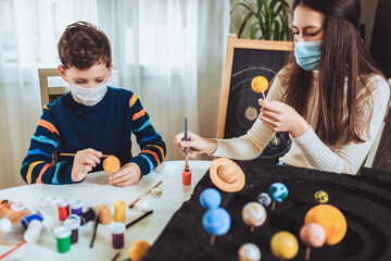 Happy school boy and girl with protective mask making a solar system for a school science project at home