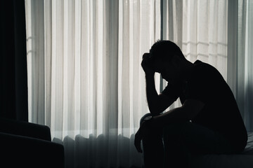 Silhouette depressed man sadly sitting on the bed in the bedroom, depression concept