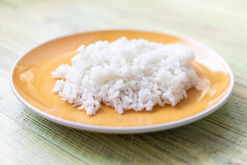 White boiled rice on a plate on a wooden background.