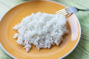 White boiled rice on a plate on a wooden background.