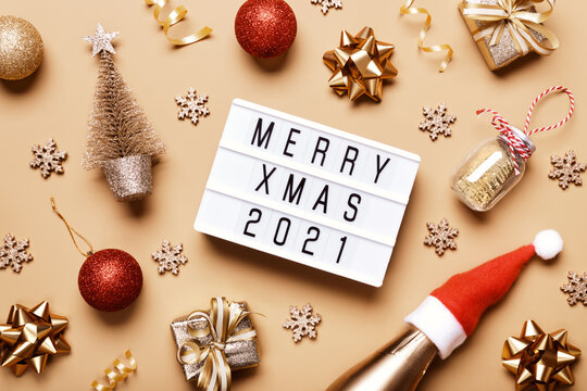 Lightbox with text MERRY XMAS 2021 and golden christmas decor on beige background. Creative layout in neutral monochrome colors