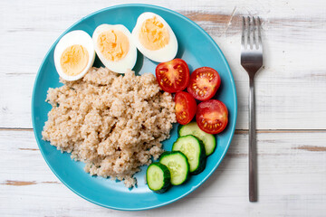 Healthy food, diet. Barley porridge, chicken eggs and vegetables on a wooden background.