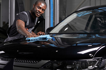 young adult afro american man cleaning car with microfiber cloth, car detailing or valeting concept