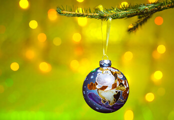 Christmas decoration - a hand-painted ball with the symbol of the Year of the Ox hanging on the Christmas tree. In the background, blurry flickering lights of a garland.