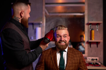 pleased elegant caucasian bearded business man getting groomed at hairdresser with hair dryer while sitting on chair at barbershop, brutal hair style concept