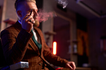 portrait of handsome adult man in a formal costume smoking a cigar, elegant guy looks confidently, has clever intelligent expression while smoking cigar