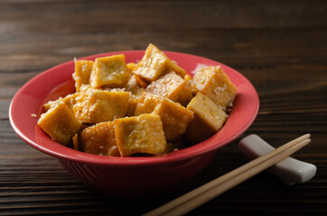 Crispy deep stir fried tofu cubes in clay dish on wooden kitchen table