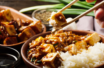 Traditional Chinese food mapo tofu dish with pork and steamed rice being held in chopsticks. Chives at background