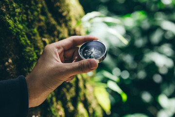 Hand of traveler holding compass in deep forest.