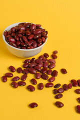 Red beans are scattered randomly and lie in a white bowl on a bright yellow background. Space for text. For advertising, for example, in healthy and organic food concepts
