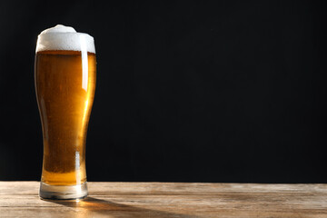 Cold tasty beer on wooden table against dark background. Space for text