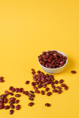 Red beans are scattered randomly and lie in a white bowl on a bright yellow background. Space for text. For advertising, for example, in healthy and organic food concepts