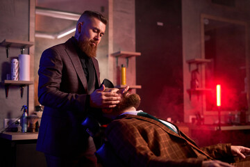 young caucasian handsome man on chair of barber having procedure of shaving, get beauty procedures in barber shop salon