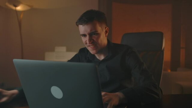 Man losing game on laptop and fury about his defeat. Hard playing and funny anger of loosing indoor of cozy flat evening apartment interior.